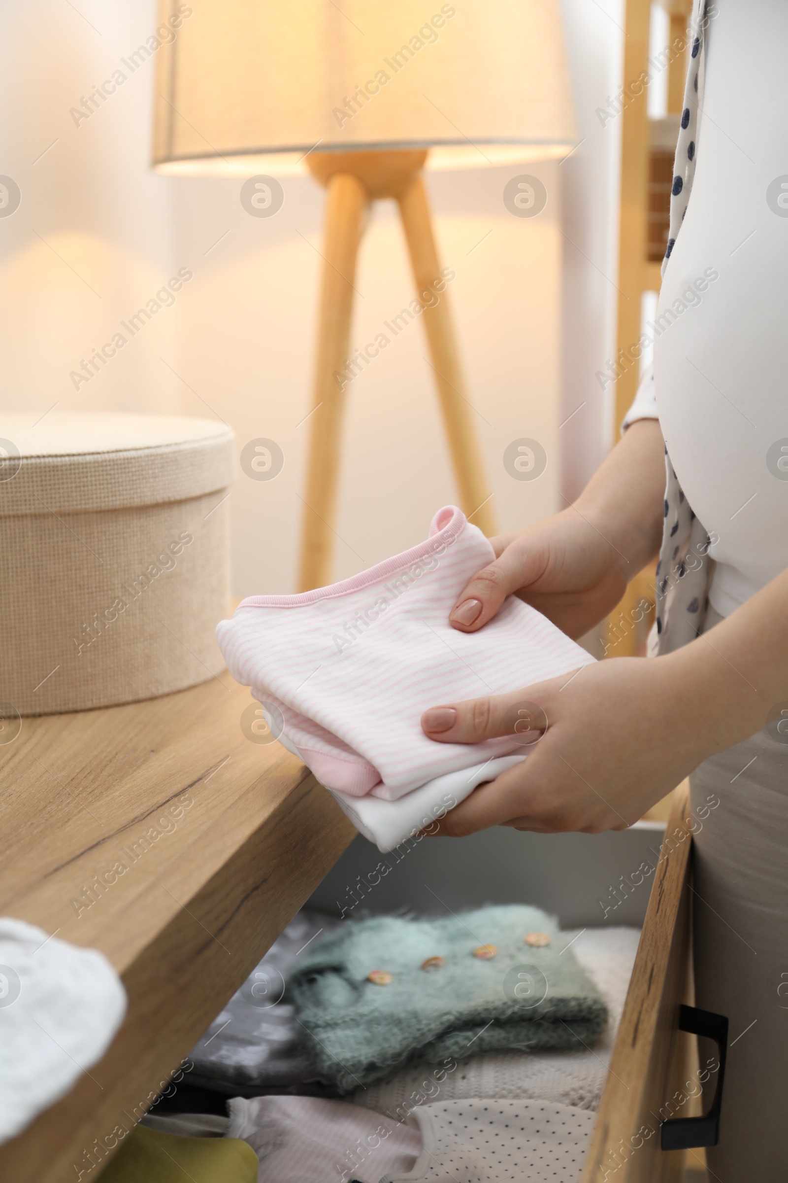 Photo of Pregnant woman with baby clothes at home, closeup