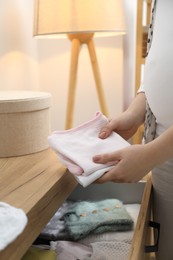 Photo of Pregnant woman with baby clothes at home, closeup