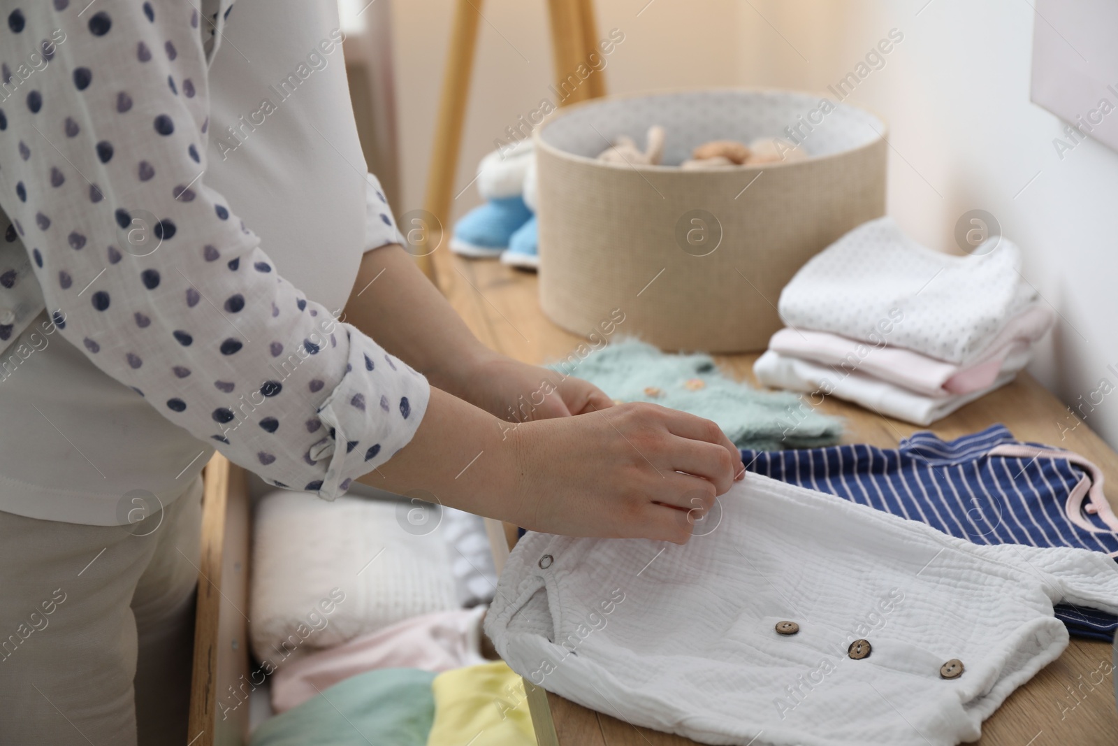 Photo of Pregnant woman with baby clothes at home, closeup