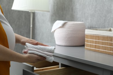 Photo of Pregnant woman with baby clothes at home, closeup