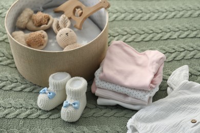 Photo of Baby clothes and box with toys on green blanket, closeup