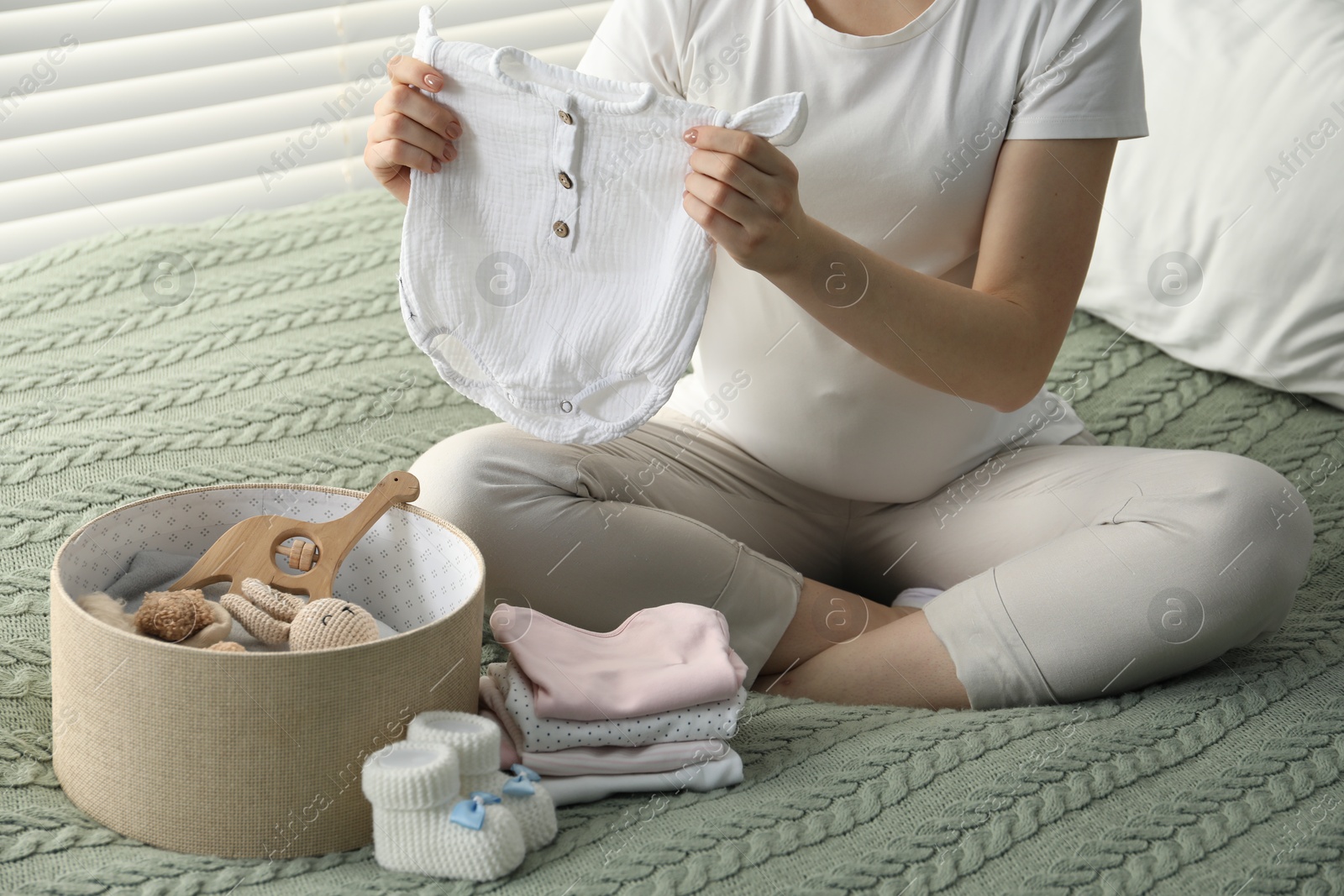 Photo of Pregnant woman with baby clothes on bed at home, closeup