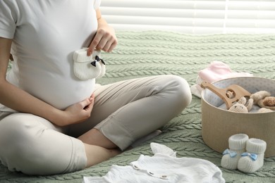 Photo of Pregnant woman with baby socks on bed at home, closeup