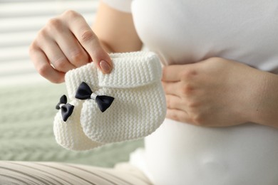 Photo of Pregnant woman with baby socks at home, closeup