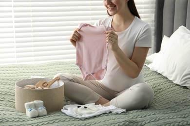 Photo of Pregnant woman with baby clothes on bed at home, closeup