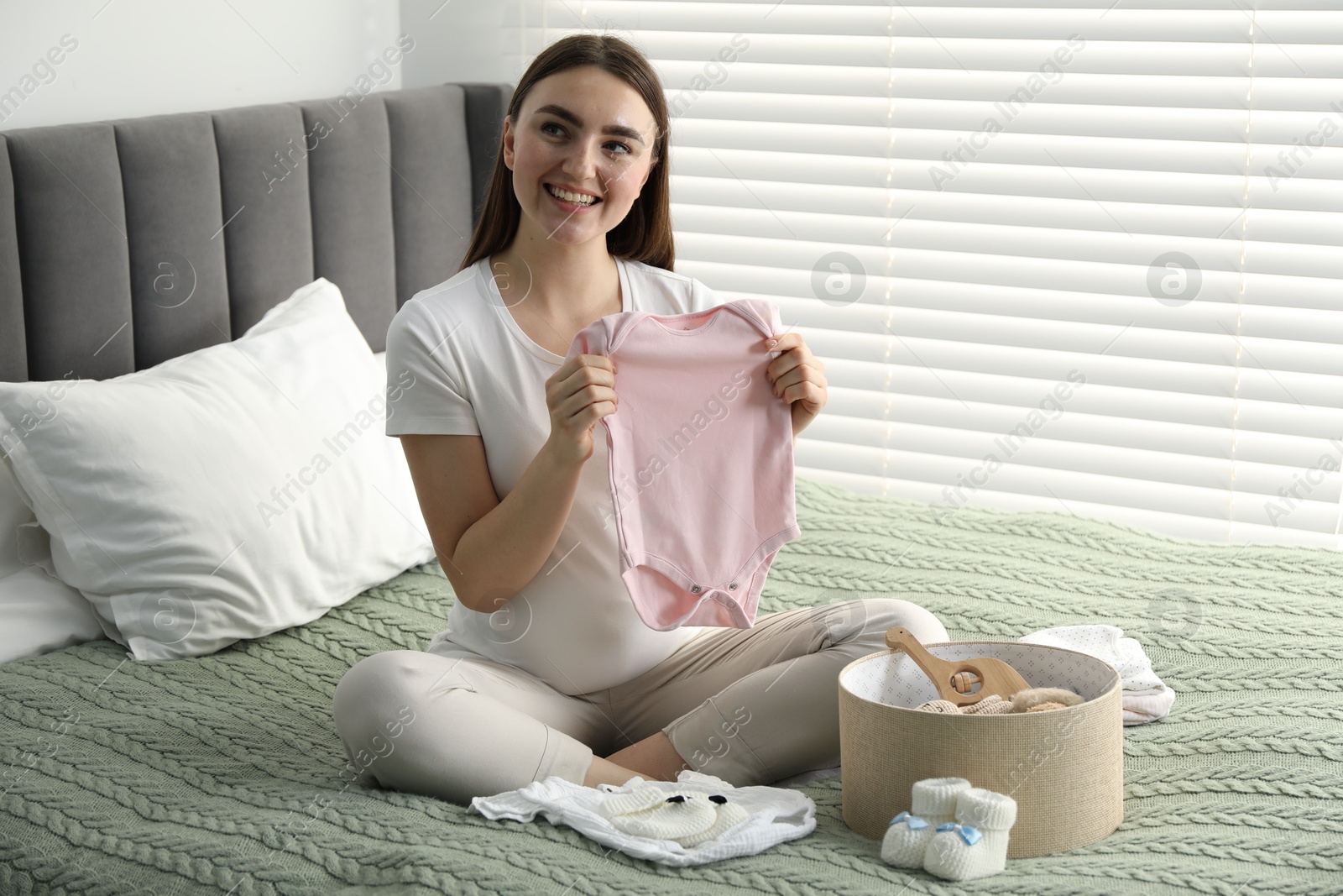 Photo of Pregnant woman with baby clothes on bed at home