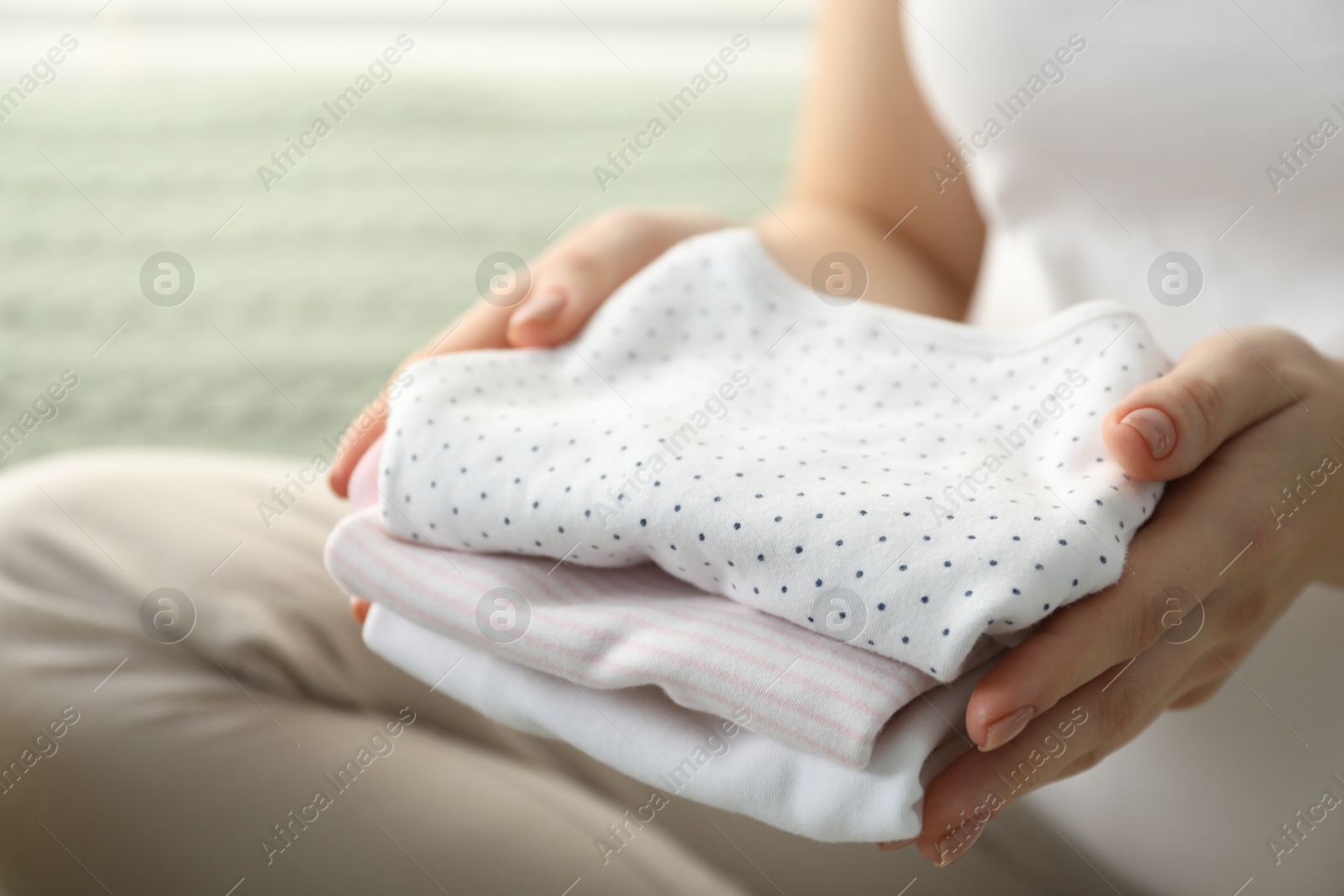 Photo of Pregnant woman with baby clothes at home, closeup