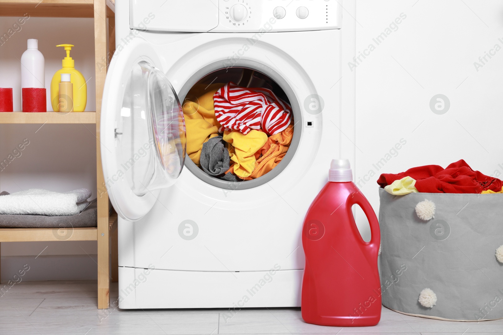 Photo of Washing machine, detergent and basket with laundry near white wall