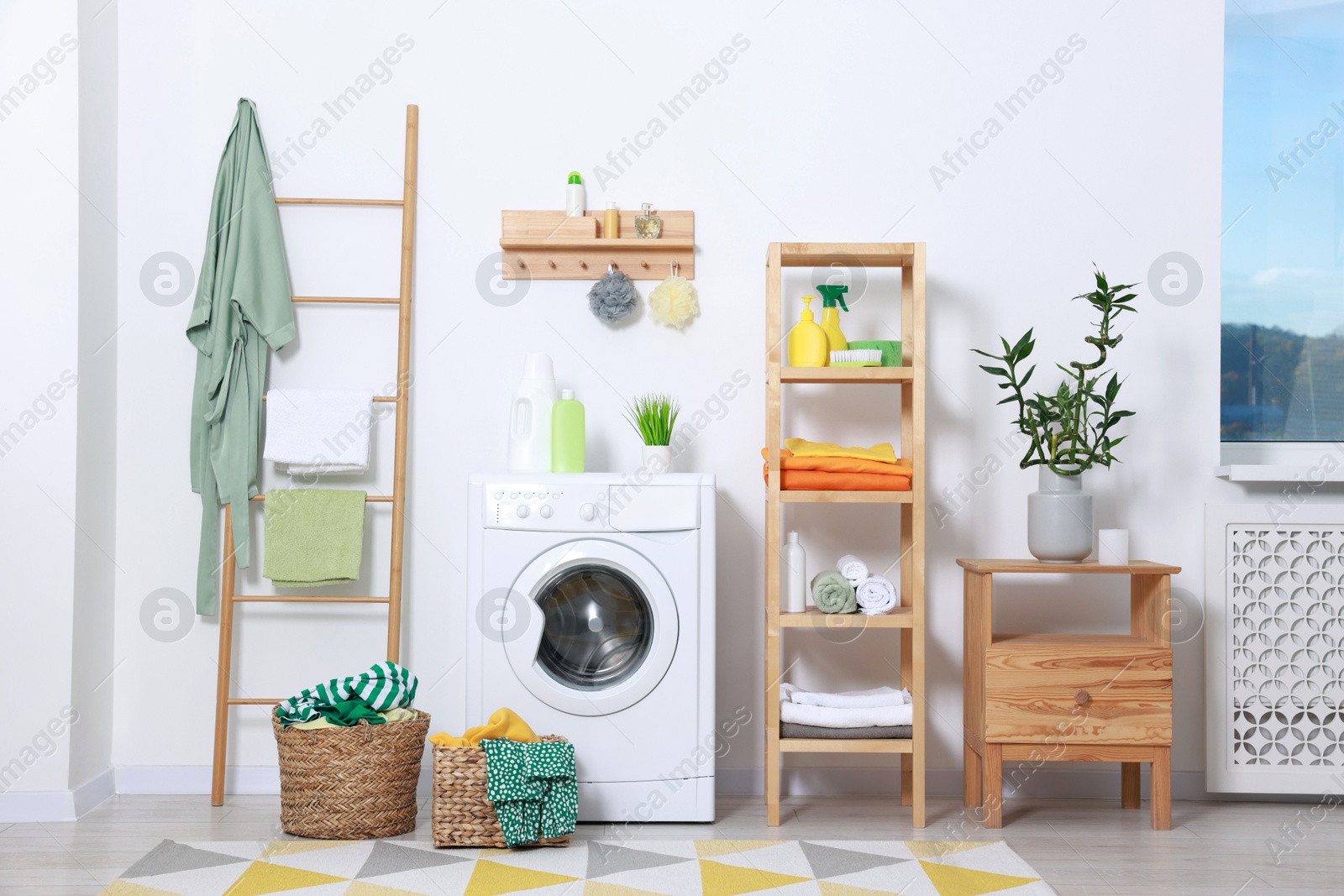 Photo of Washing machine, detergents, bathrobe and basket with laundry in room