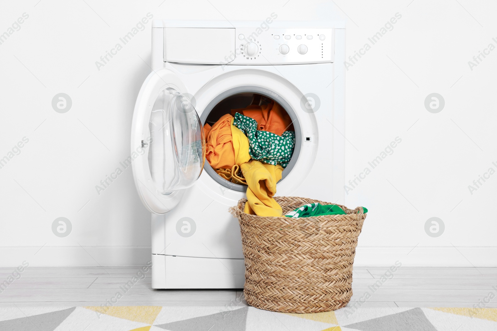 Photo of Modern washing machine with clothes and laundry basket near white wall