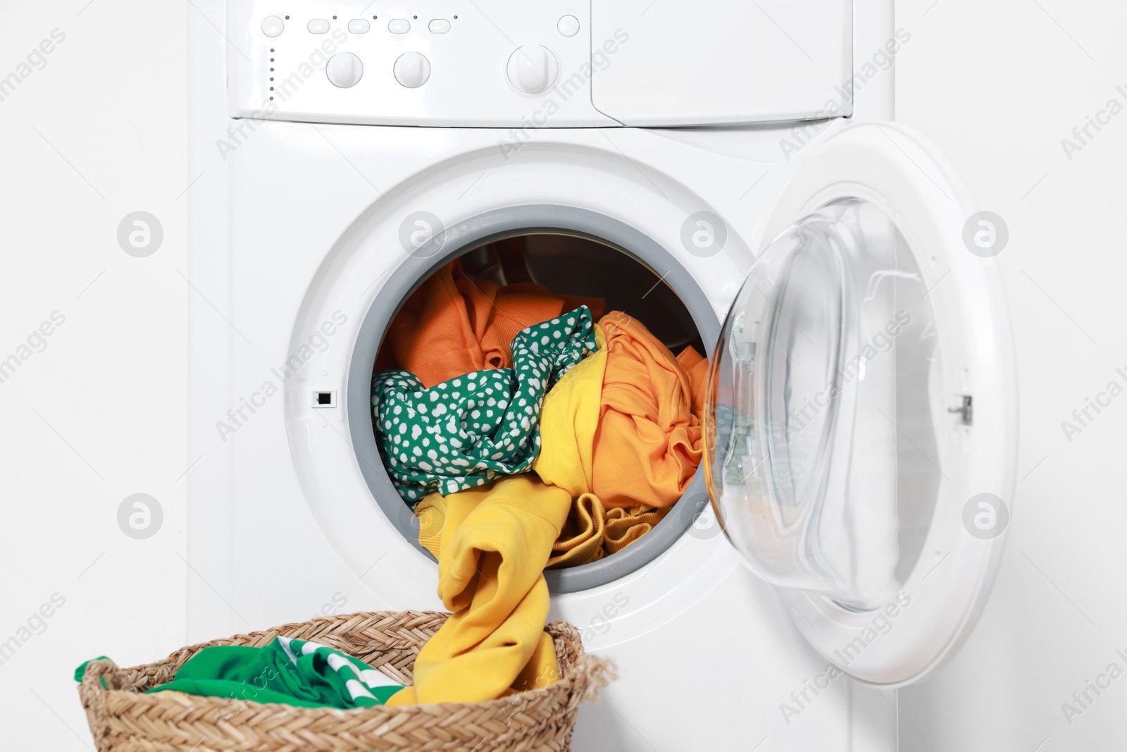 Photo of Modern washing machine with clothes and laundry basket near white wall