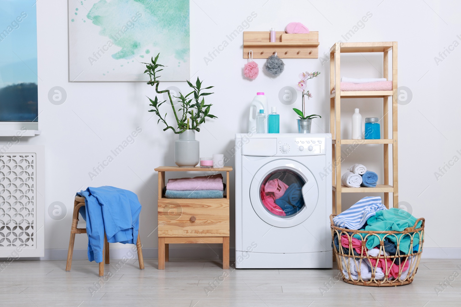 Photo of Washing machine, detergents, clean towels and basket with laundry in room