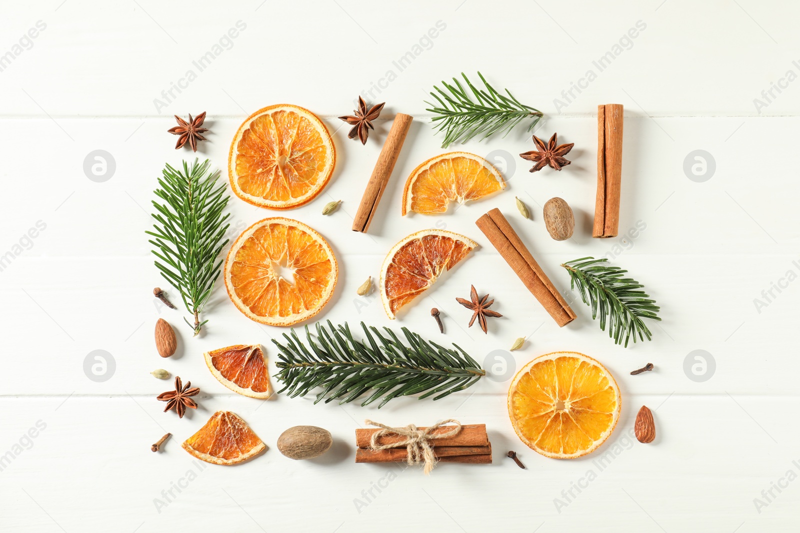 Photo of Different spices, dried orange slices and fir tree branches on white wooden table, flat lay. Christmas season