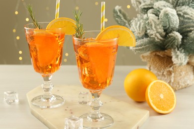 Photo of Tasty Christmas cocktail in glasses and fir tree branches on white wooden table against blurred lights, closeup