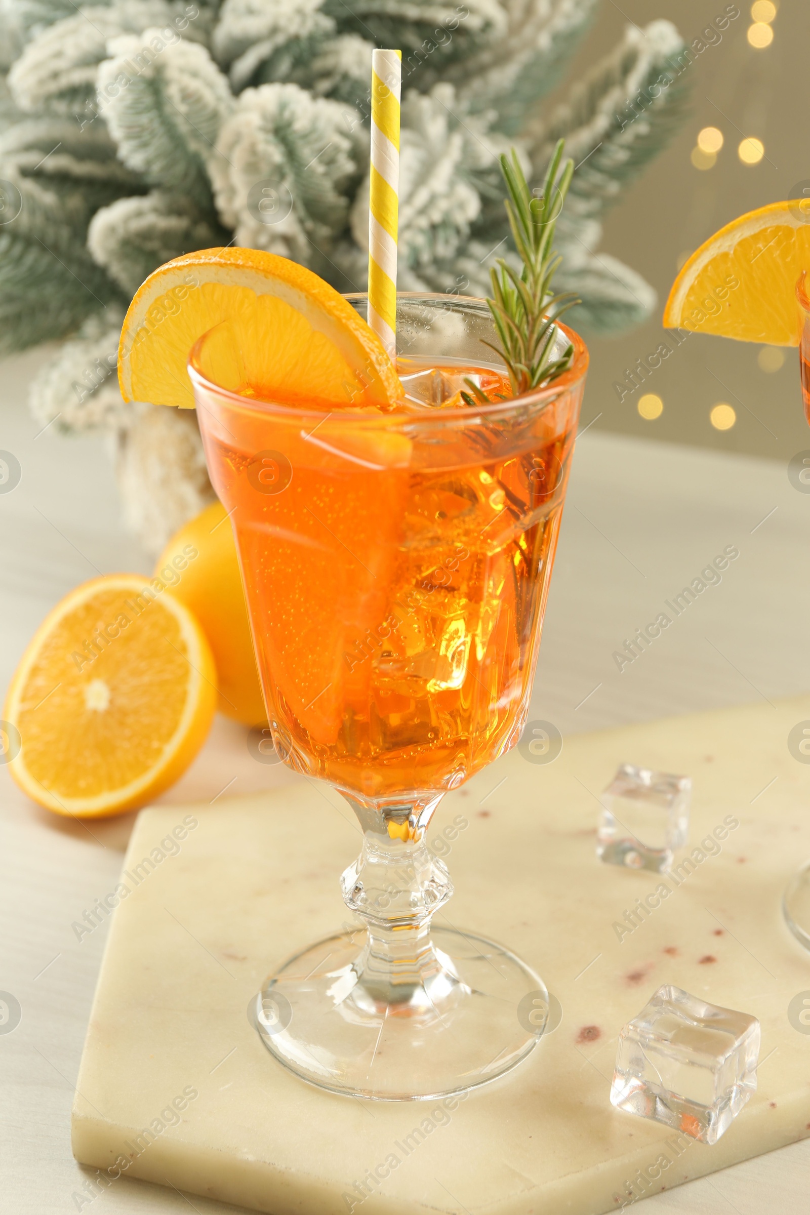 Photo of Tasty Christmas cocktail in glass and fir tree branches on white wooden table against blurred lights, closeup