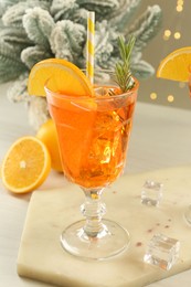 Photo of Tasty Christmas cocktail in glass and fir tree branches on white wooden table against blurred lights, closeup