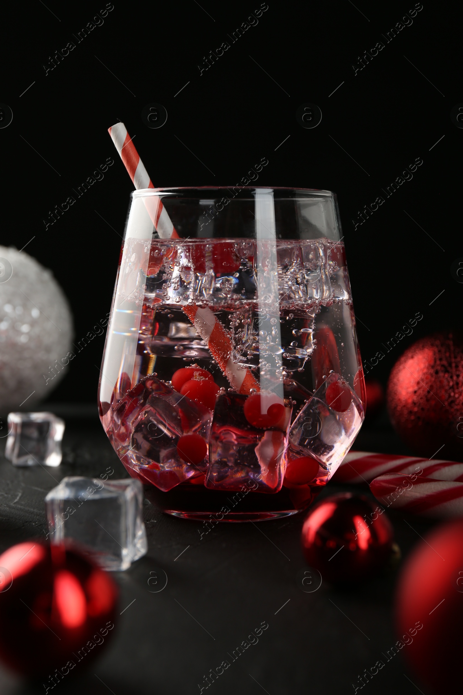 Photo of Tasty Christmas cocktail in glass, ice cubes and decor on black table, closeup