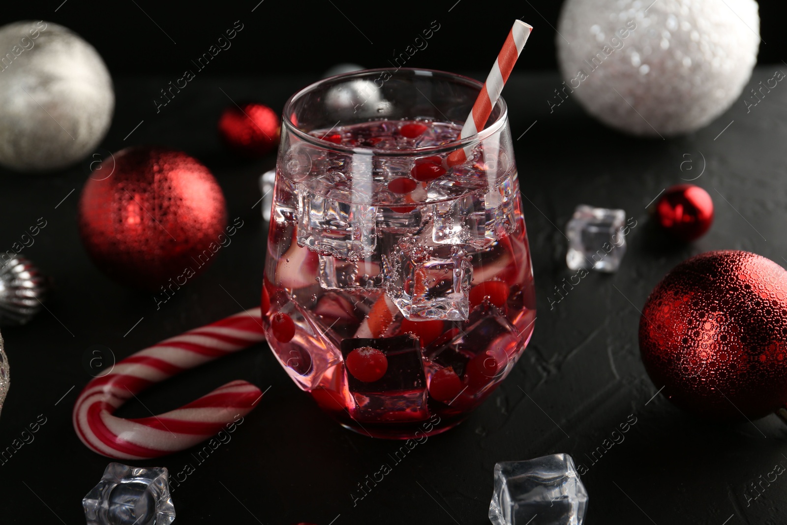 Photo of Tasty Christmas cocktail in glass, ice cubes and decor on black table, closeup