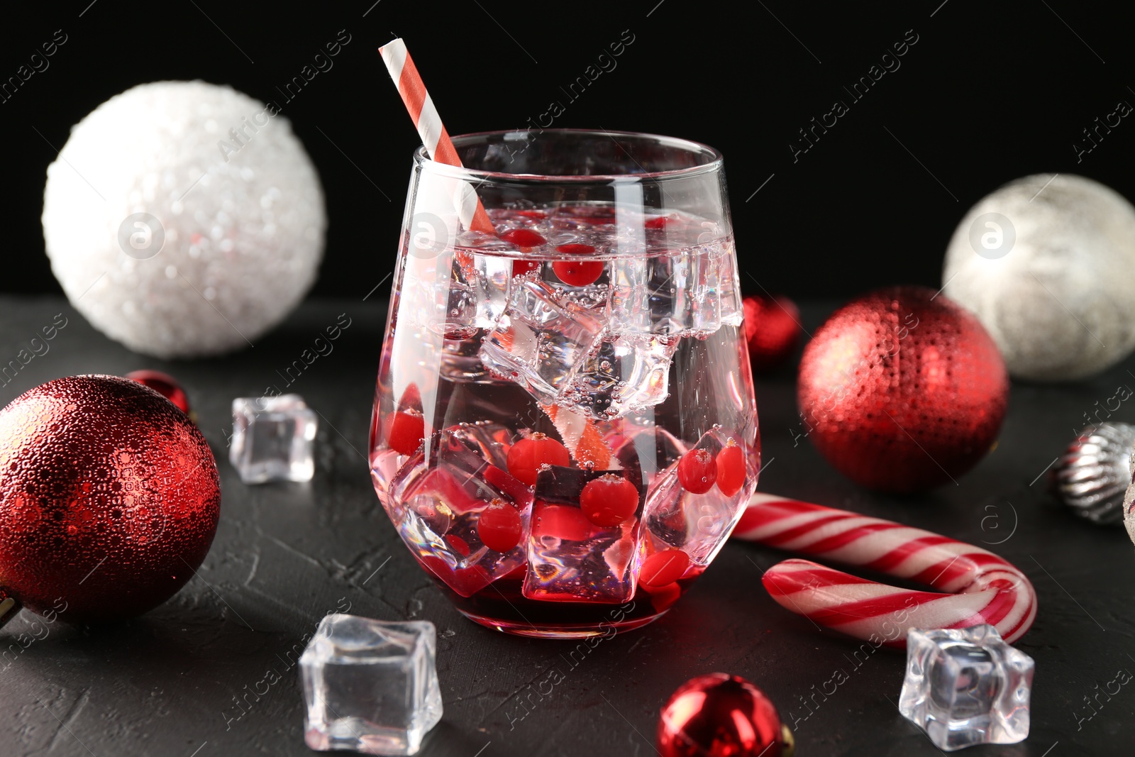 Photo of Tasty Christmas cocktail in glass, ice cubes and decor on black table, closeup