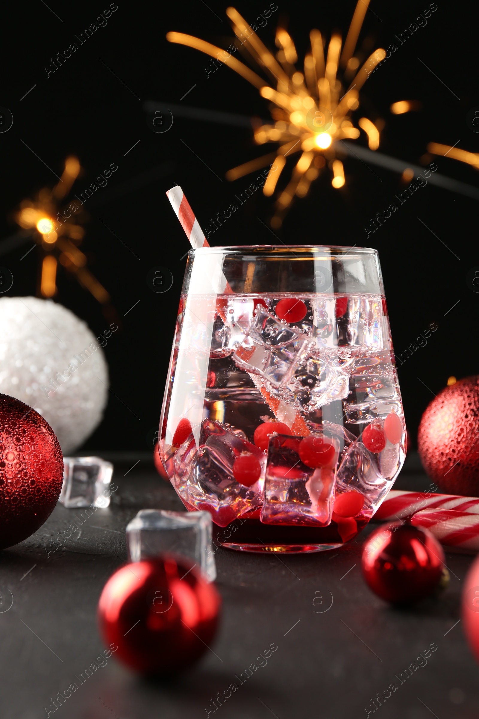 Photo of Tasty Christmas cocktail in glass, ice cubes and decor on black table, closeup