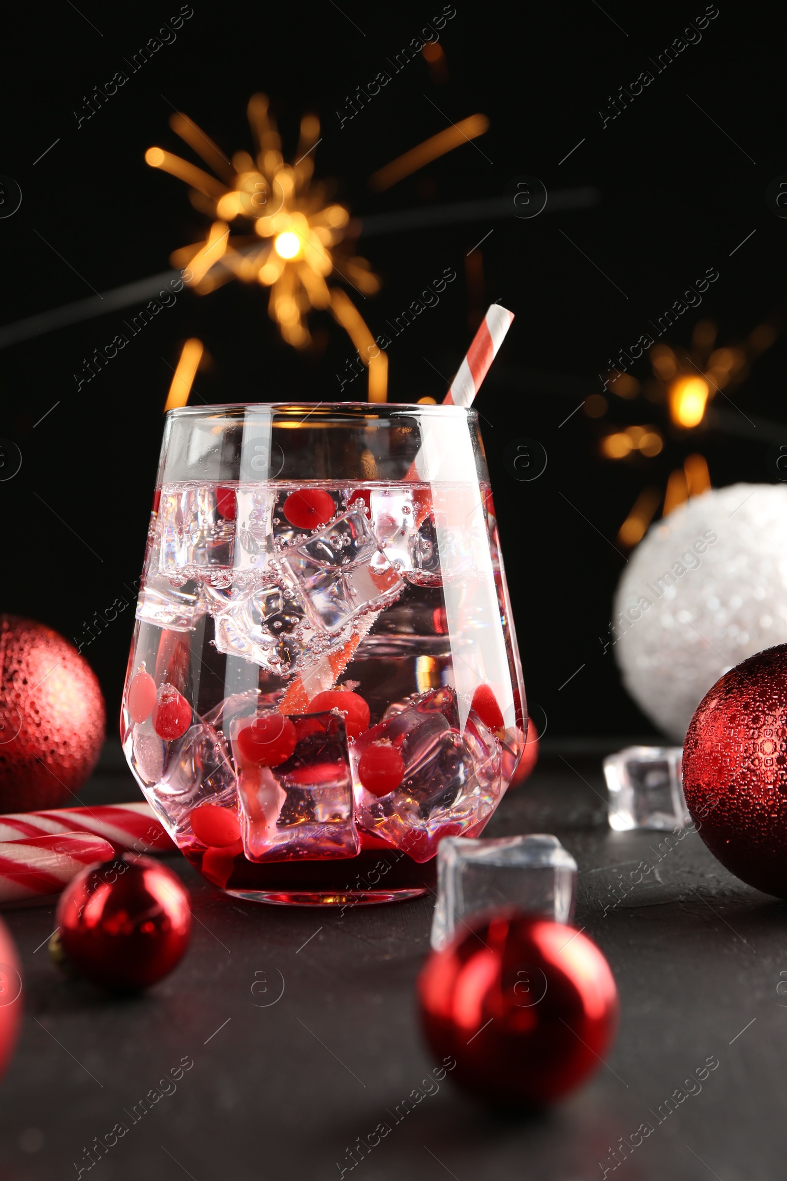 Photo of Tasty Christmas cocktail in glass, ice cubes and decor on black table, closeup