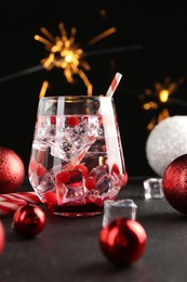 Photo of Tasty Christmas cocktail in glass, ice cubes and decor on black table, closeup