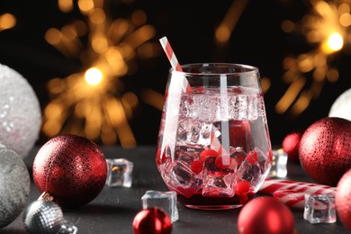 Photo of Tasty Christmas cocktail in glass, ice cubes and decor on black table against blurred lights, closeup