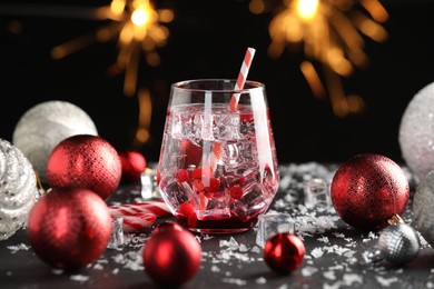 Photo of Tasty Christmas cocktail in glass, ice and decor on table against dark background with blurred lights