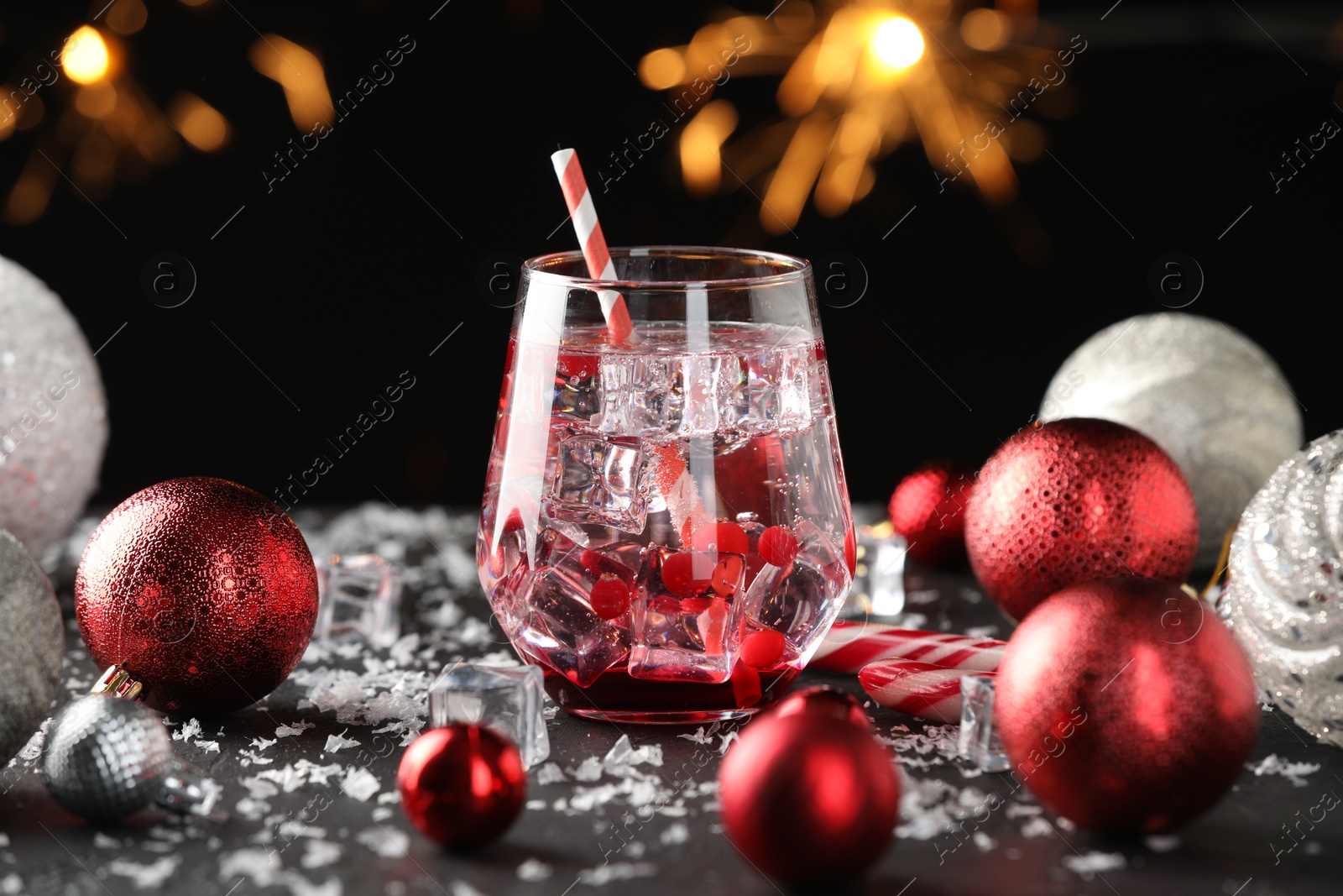 Photo of Tasty Christmas cocktail in glass, ice and decor on table against dark background with blurred lights