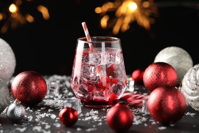 Photo of Tasty Christmas cocktail in glass, ice and decor on table against dark background with blurred lights