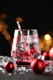 Photo of Tasty Christmas cocktail in glass, ice and decor on table against dark background with blurred lights, closeup