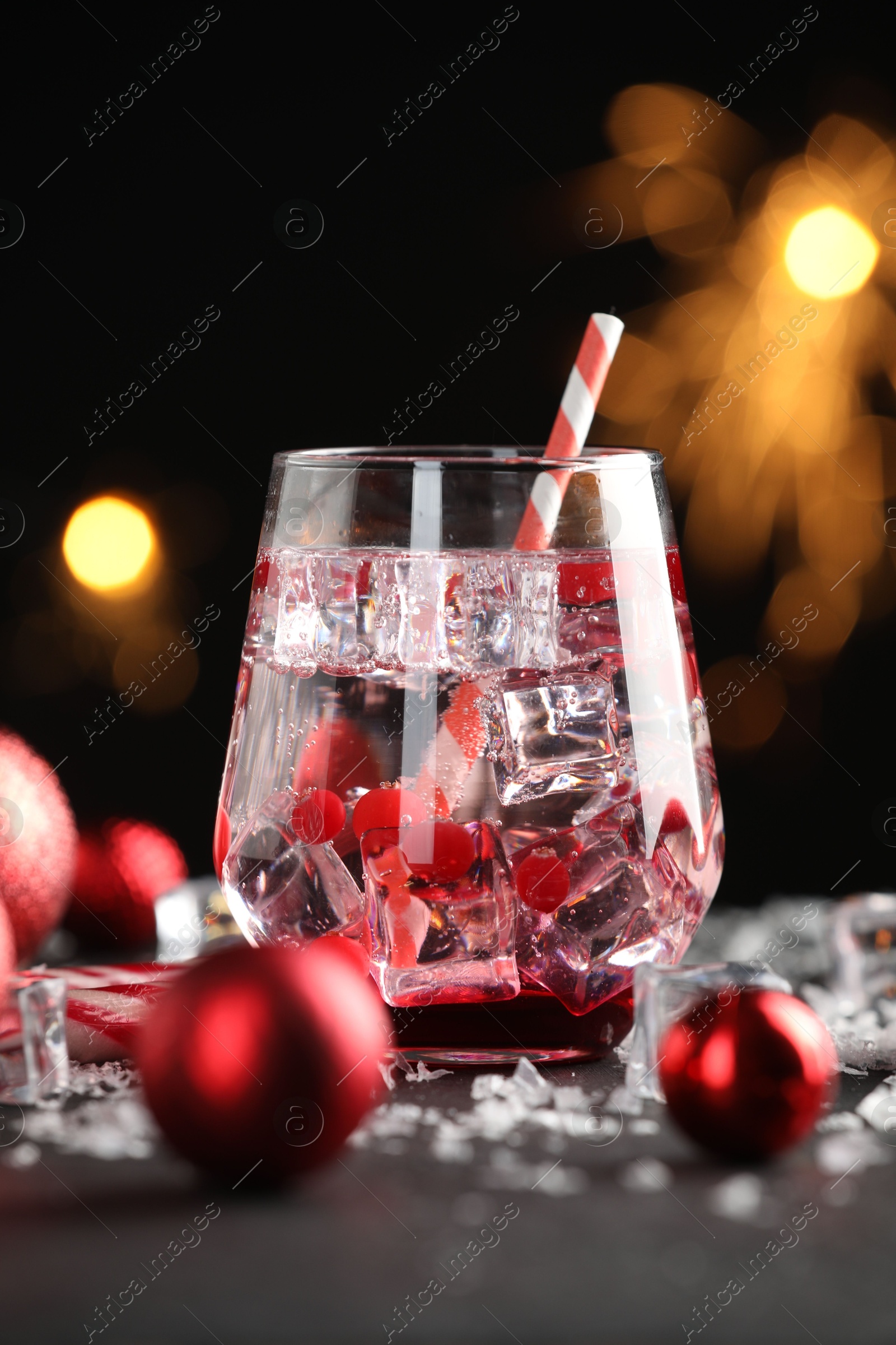 Photo of Tasty Christmas cocktail in glass, ice and decor on table against dark background with blurred lights, closeup