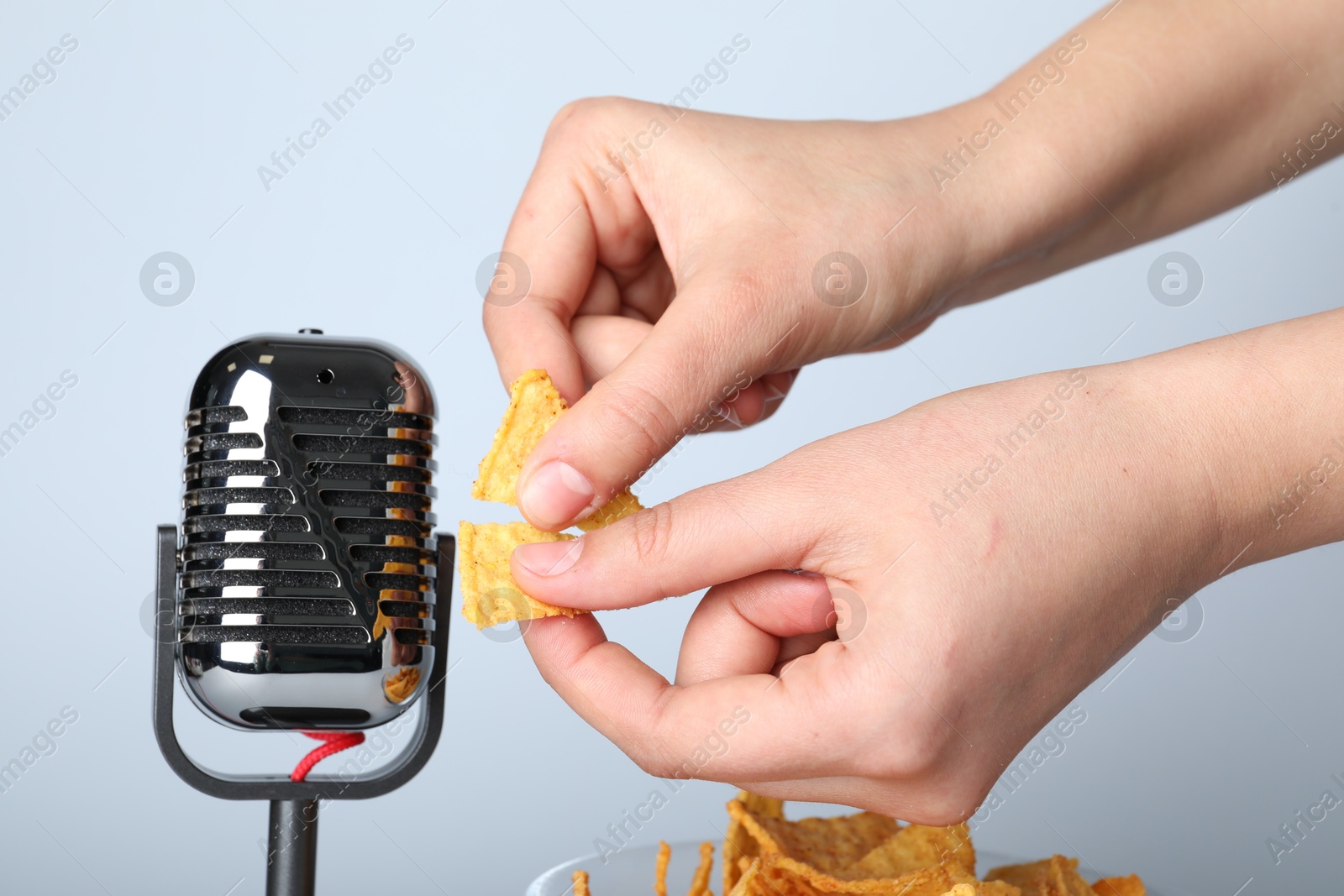 Photo of Woman making ASMR sounds with microphone and nacho chip on grey background, closeup