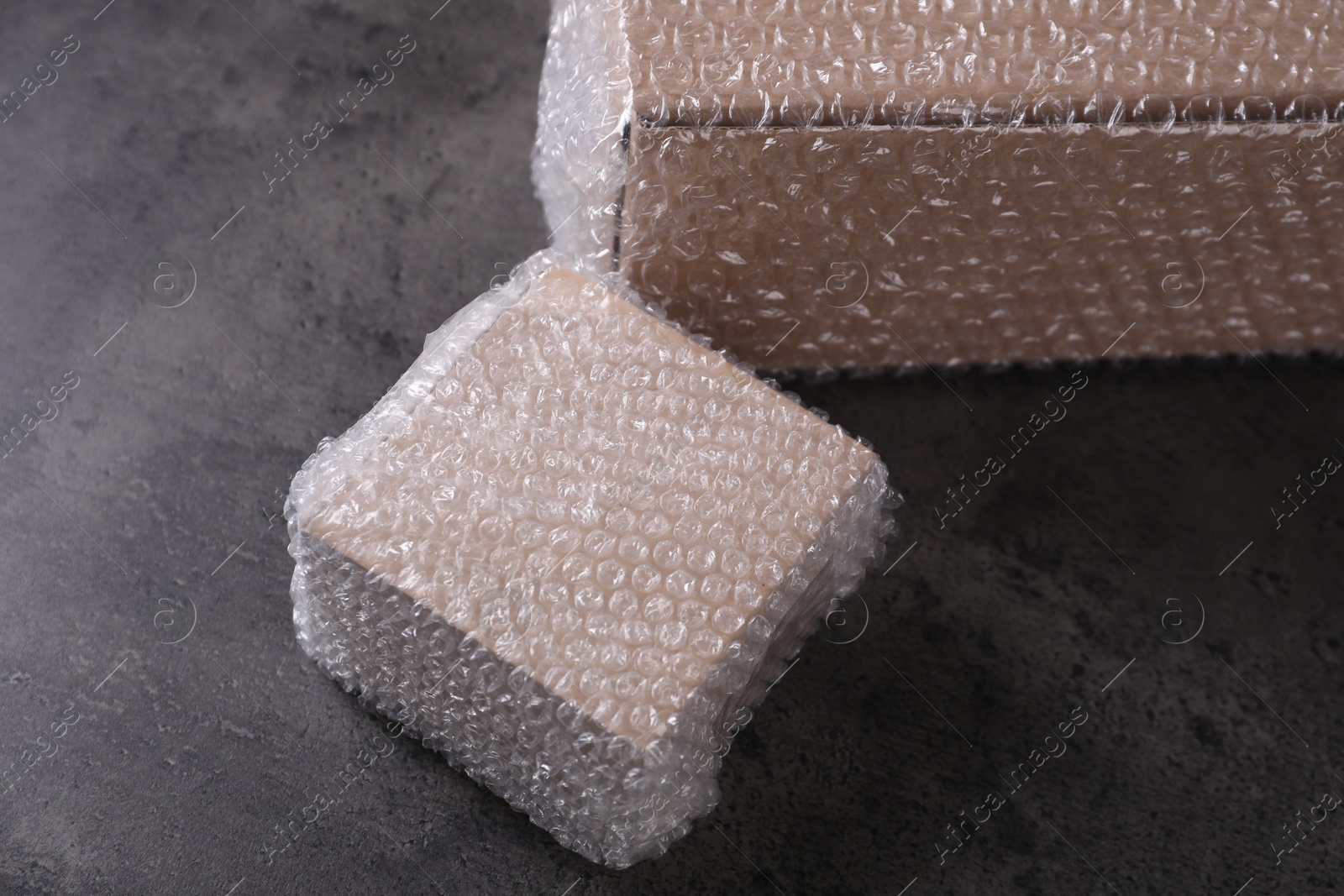 Photo of Cardboard boxes covered with bubble wrap on dark grey table