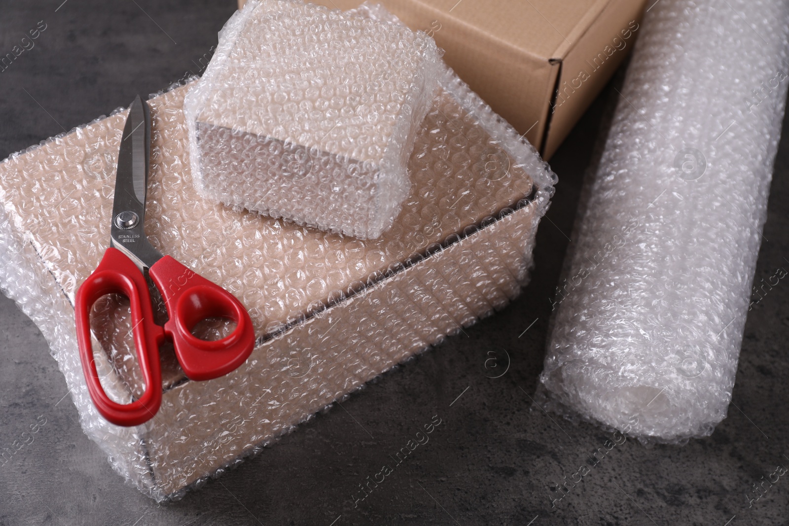 Photo of Cardboard boxes, bubble wrap and scissors on dark grey table