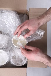 Photo of Man covering ceramic dishware with bubble wrap, closeup