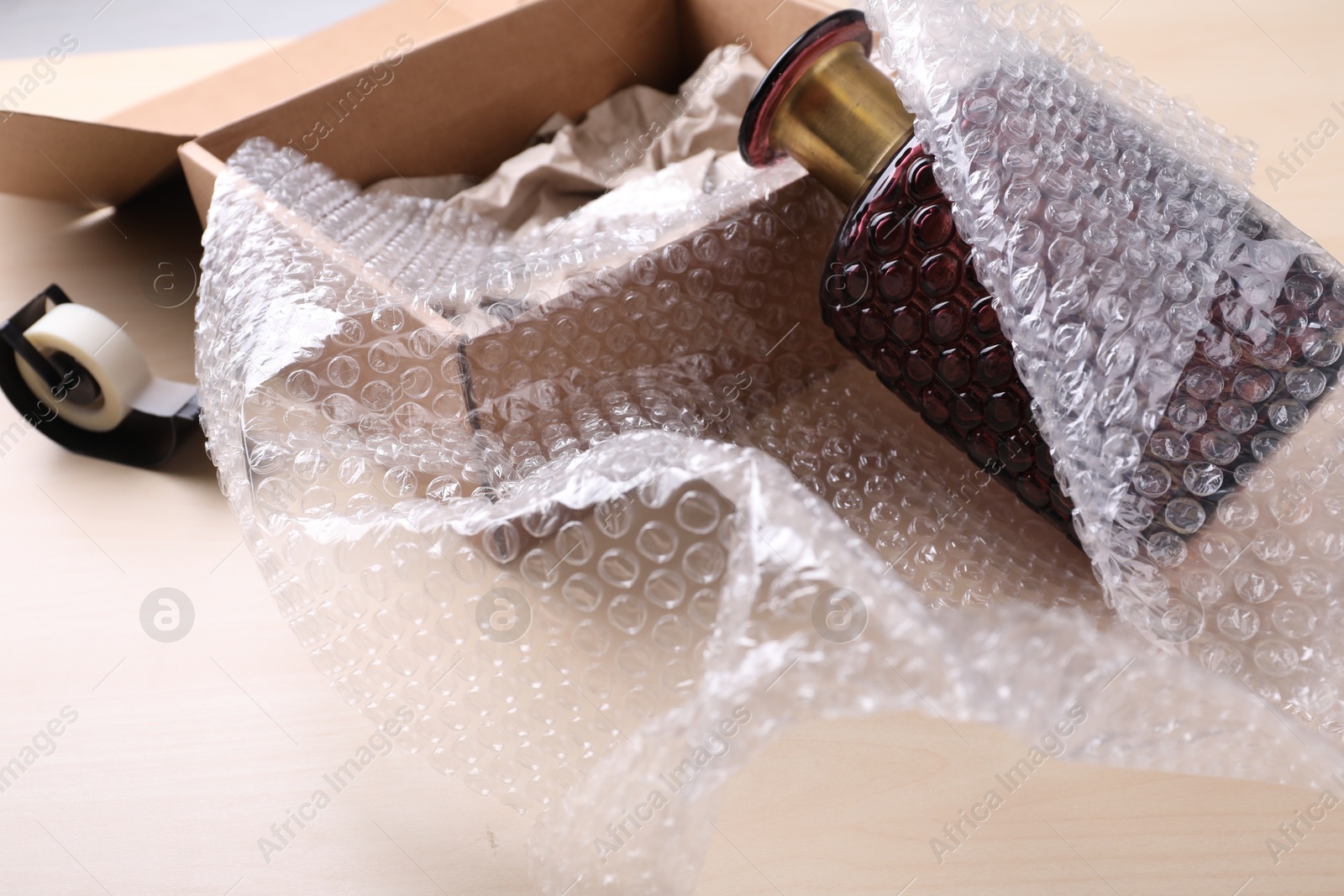 Photo of Beautiful glass vase in bubble wrap near cardboard box and adhesive tape on wooden table