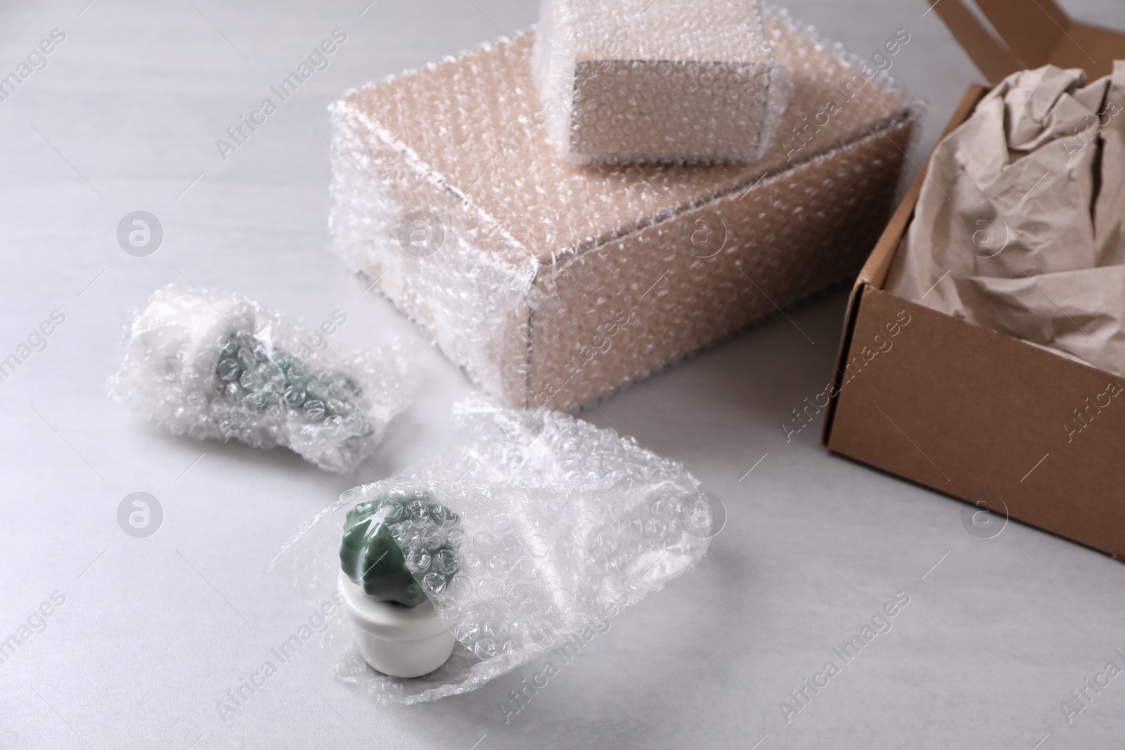 Photo of Fragile ceramic decor elements in bubble wrap near cardboard boxes on light grey table