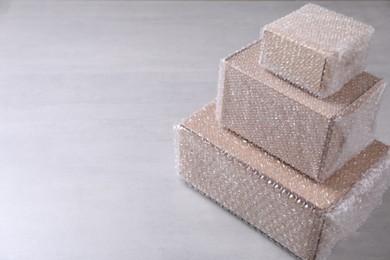 Photo of Cardboard boxes covered with bubble wrap on light grey table. Space for text