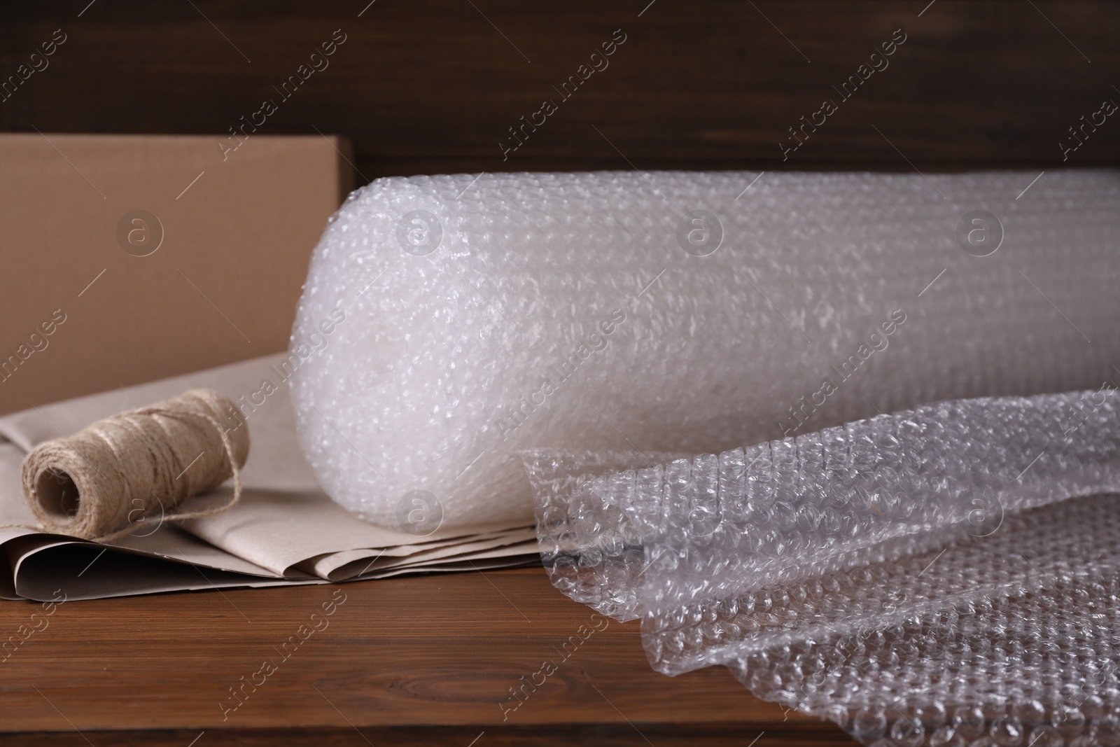 Photo of Twine, paper and roll of bubble wrap on wooden table