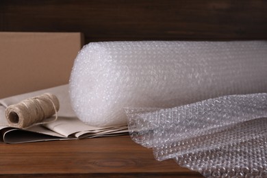 Photo of Twine, paper and roll of bubble wrap on wooden table