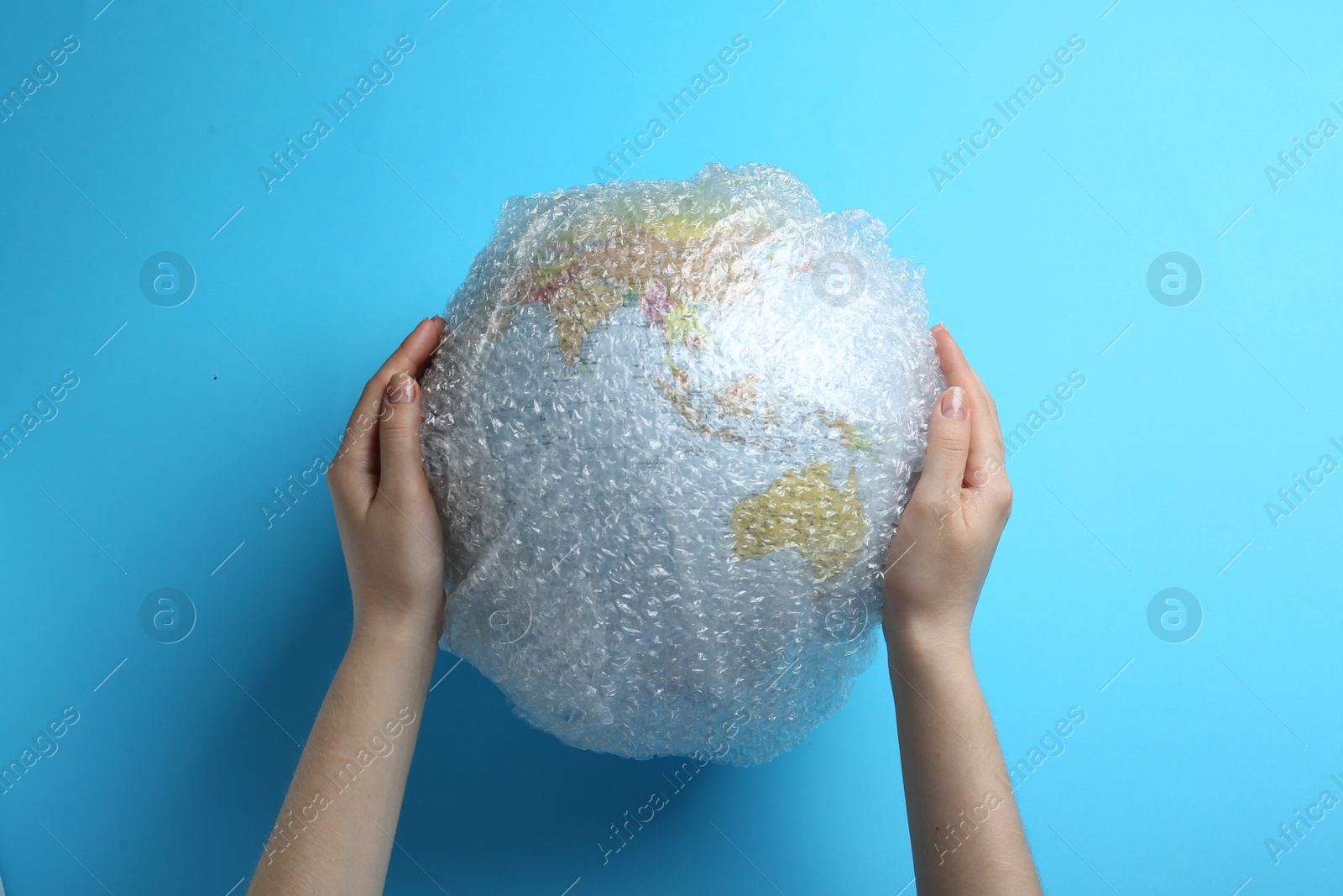 Photo of Woman holding globe packed in bubble wrap on turquoise background, top view. Environmental conservation