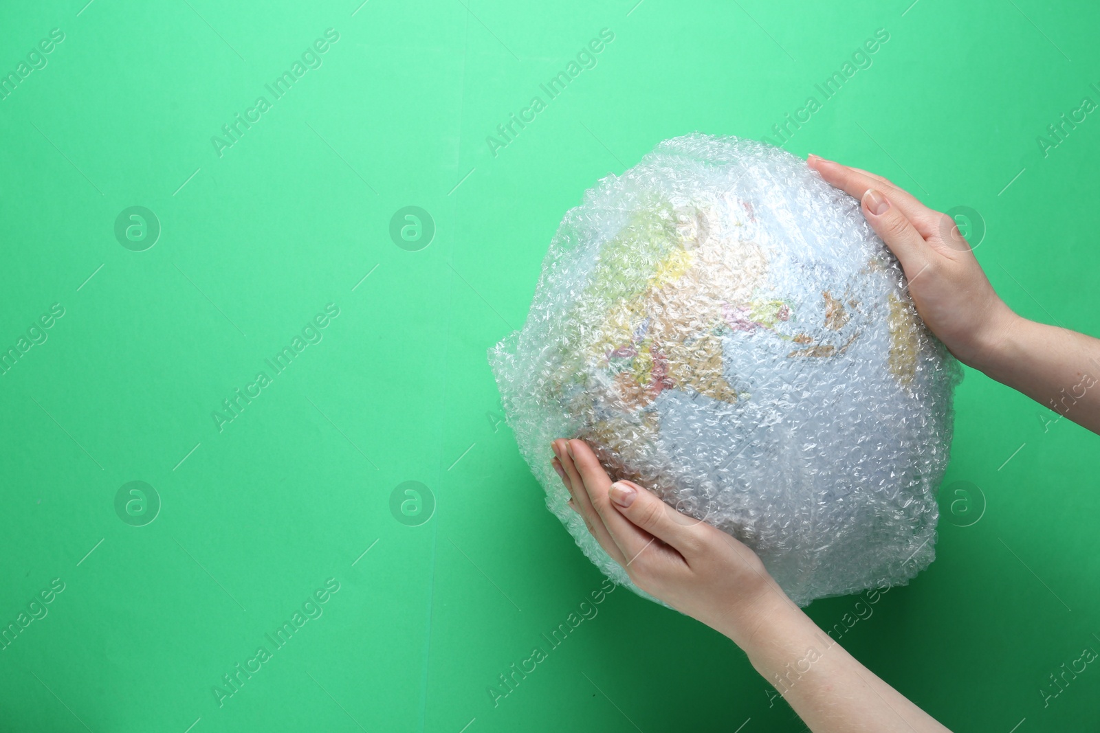 Photo of Woman holding globe packed in bubble wrap and space for text on light green background, top view. Environmental conservation