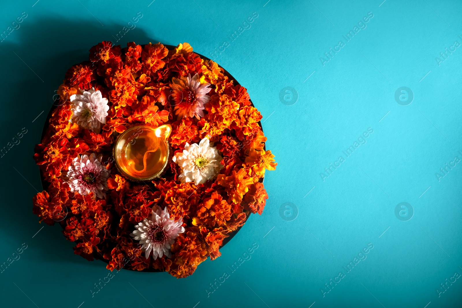 Photo of Diwali celebration. Diya lamp and beautiful flowers on turquoise background, top view. Space for text