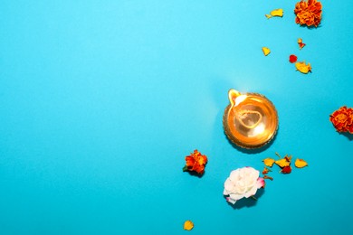 Photo of Diwali celebration. Diya lamp and beautiful flowers on turquoise background, top view. Space for text