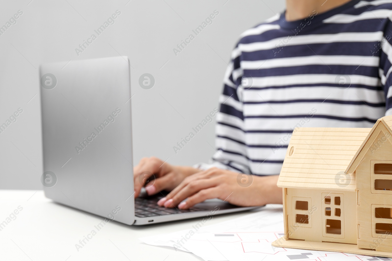 Photo of House hunting. Woman with laptop, papers and house figure at white table, closeup