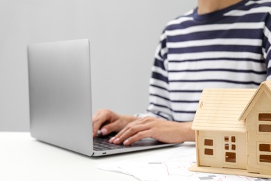 Photo of House hunting. Woman with laptop, papers and house figure at white table, closeup