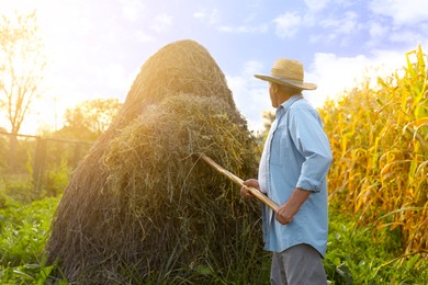 Photo of Senior man in straw hat pitching hay on farmland