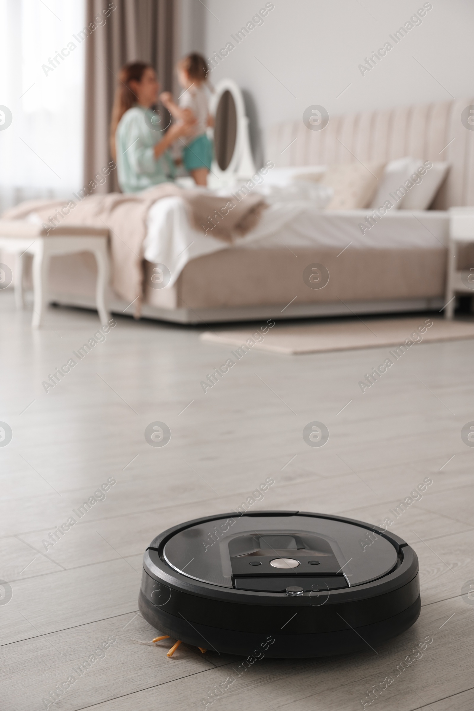 Photo of Mother spending time with her daughter in bedroom, focus on robotic vacuum cleaner