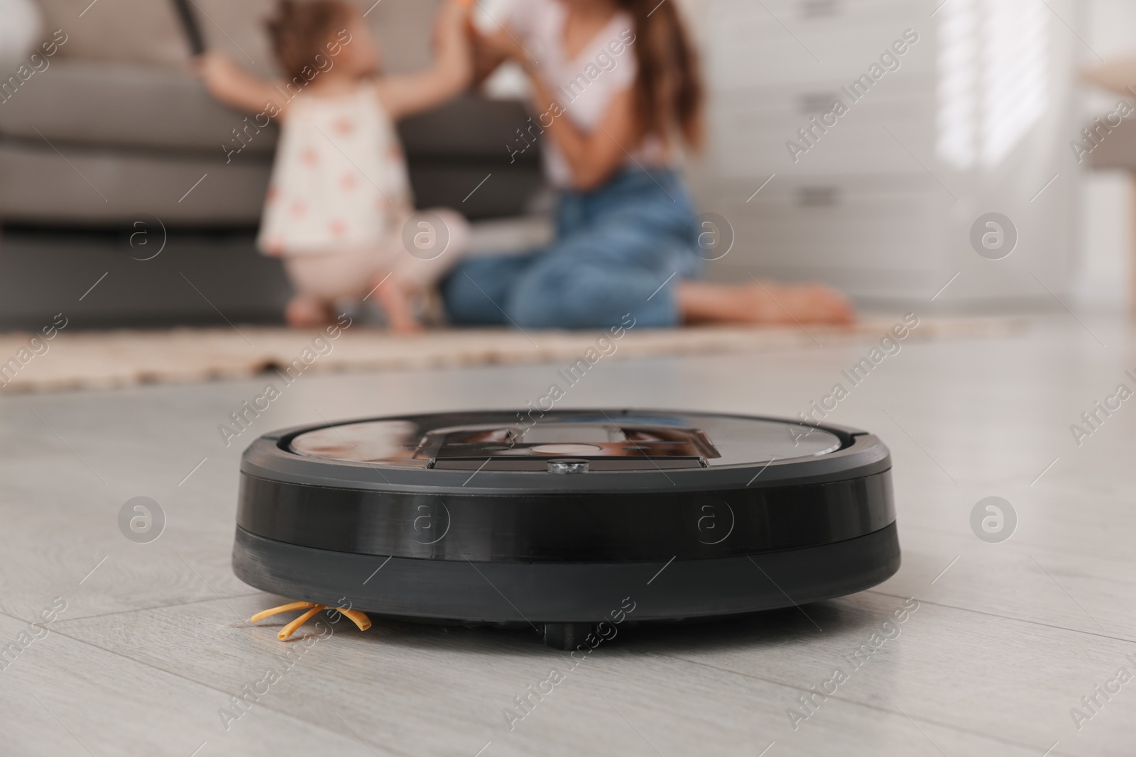 Photo of Mother spending time with her daughter in room, focus on robotic vacuum cleaner